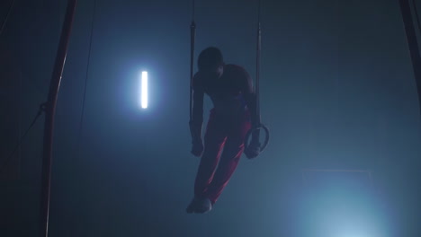 male-gymnast-athlete-performs-handstand-and-rotation-on-rings-on-dark-background-and-smoke-in-slow-motion