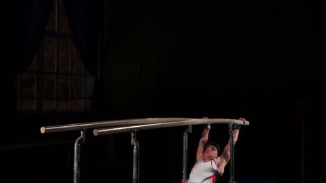 Male-gymnast-acrobat-performs-handstand-on-parallel-bars-in-a-dark-room-in-slow-motion