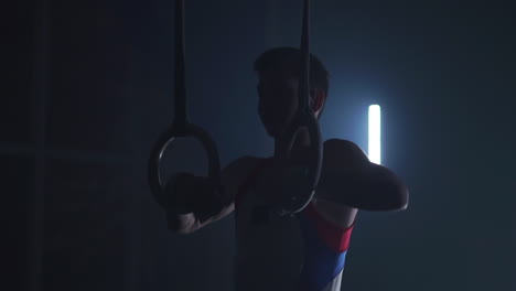 Gymnast-on-a-dark-background-stands-on-his-hands-using-rings-in-the-air.-Performs-rotation-in-the-Olympic-program-in-slow-motion-120-fps.-gymnastic-rings,-professional-gymnast