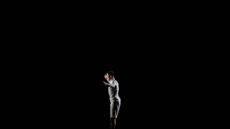Handsome-male-professional-gymnast-in-white-clothes-on-a-black-background-performs-at-the-gymnastics-competition-and-performs-exercises-on-the-trampoline-jumping-somersaults.