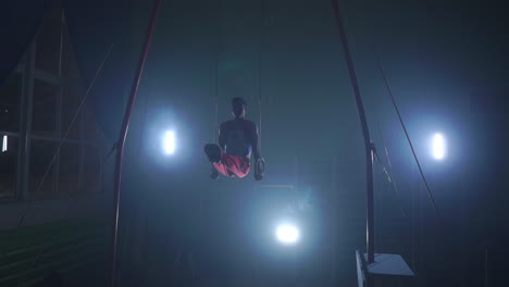 male-gymnast-athlete-performs-handstand-and-rotation-on-rings-on-dark-background-and-smoke-in-slow-motion