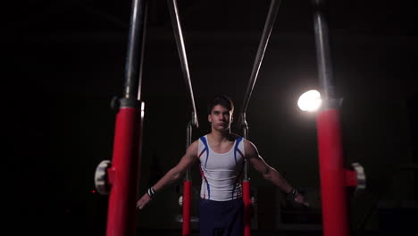 Professional-gymnast-in-a-dark-room-in-sportswear-stands-on-crayfish-on-parallel-bars-and-performs-flips-in-slow-motion