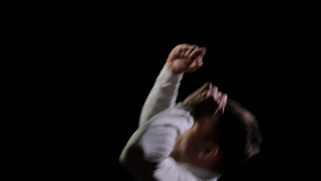 Athletic-man-in-white-clothes-performs-tricks-jumping-on-a-trampoline-on-a-black-monophonic-background