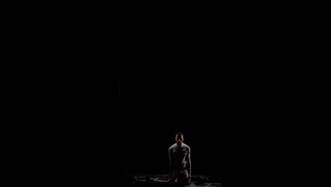 male-gymnast-on-a-black-background-in-white-clothes-soars-into-the-frame-from-below-and-makes-rotation-in-the-air-and-flips-in-slow-motion.-Gymnast-in-the-competition.-Individual-skill,-flight-and-concentration