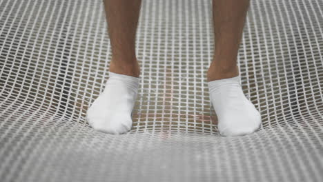 Nahaufnahme-Von-Füßen-In-Weißen-Socken,-Die-Auf-Dem-Trampolingitter-Stehen-Und-In-Zeitlupe-Schwingen,-Um-Zu-Springen.-Der-Beginn-Der-Rede.