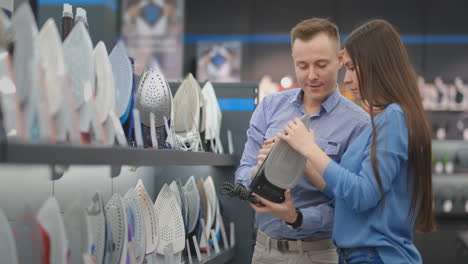 Beautiful-married-couple-buys-a-new-iron-for-their-home.-Hold-the-iron-in-the-store-to-study-the-characteristics.-Stand-at-the-counter-with-electrical-appliances