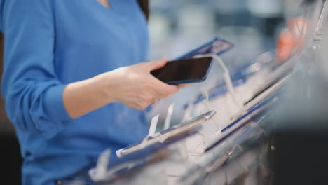 Close-up-of-a-woman-in-an-electronics-store-holding-in-her-hands-two-new-smartphone-and-chooses-the-best-one-standing-near-the-showcase-with-gadgets