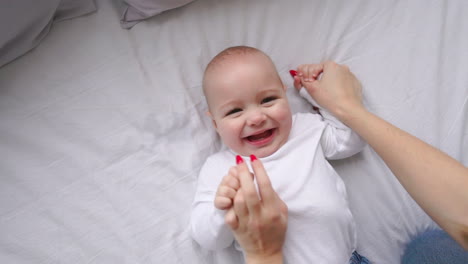 Baby-in-white-t-shirt-lying-on-a-white-bed-and-laughing-looking-at-the-camera-top-view-slow-motion
