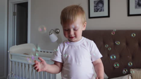 A-boy-in-a-white-T-shirt-and-blue-jeans-catches-soap-bubbles-standing-on-the-bed-in-the-parent-bedroom