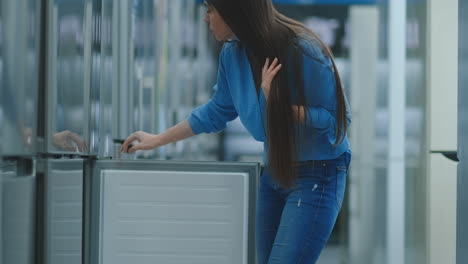 Eine-Junge-Frau-öffnet-Die-Kühlschranktür,-Um-Geräte-Aufzubewahren-Und-Mit-Anderen-Modellen-Zu-Vergleichen,-Um-Das-Neue-Haus-Zu-Kaufen