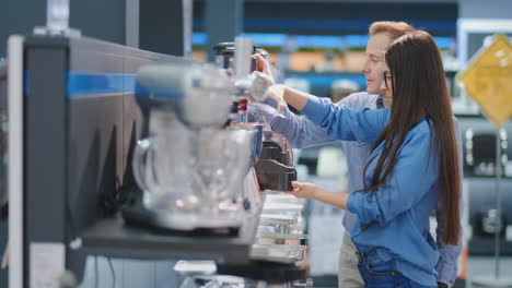 Young-beautiful-woman-in-the-appliances-store-is-choosing-for-its-kitchen-a-blender-looking-and-holding-in-her-hands-various-models.