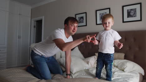 Dad-plays-with-his-son-in-the-bedroom-catching-soap-bubbles-smiling-and-laughing