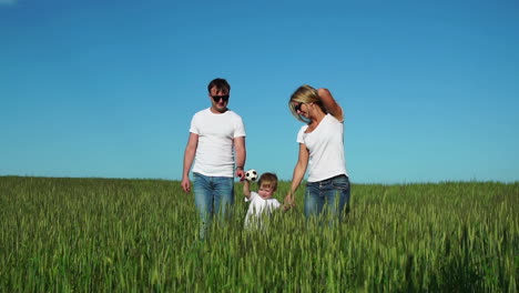 Mother-father-and-son-walk-in-the-field-with-spikes-in-white-t-shirts-and-jeans-smiling-cheerfully-at-each-other