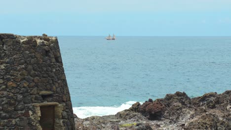 Wooden-sailboat-near-Tenerife-island-in-distance,-rocky-building-in-foreground