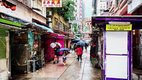 Leichter-Regen-über-Fußgängern-Mit-Sonnenschirmen,-Die-Tagsüber-Auf-Der-Tai-Yuen-Straße-In-Wan-Chai-Spazieren