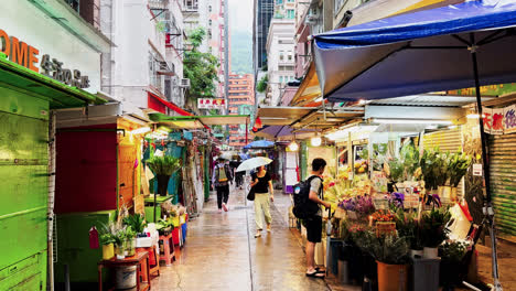 Los-Peatones-Con-Sombrillas-Pasan-Por-Puestos-Callejeros-Abiertos-En-La-Calle-Tai-Yuen-En-Wan-Chai,-Hong-Kong