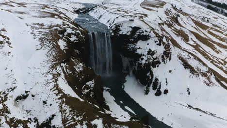 Aerial-view-around-the-snowy-Skogafoss-waterfall,-cloudy,-winter-day-in-Iceland