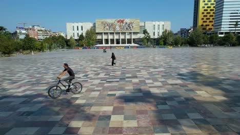 People-walking-and-cycling-on-center-of-Tirana-capital-in-a-sunny-day,-beautiful-paved-square-with-colorful-marble
