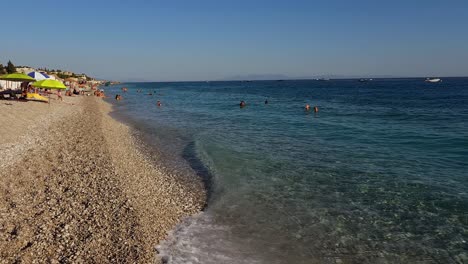 Beach-of-Drymades-in-Albania,-full-of-people-sunbathe-and-enjoy-clear-blue-water-of-Ionian-sea-on-summer-vacation