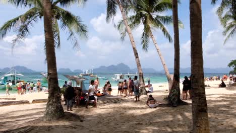 People-on-busy-white-sandy-beach-of-popular-tourist-destination-of-Seven-Commandos-during-island-hopping-tour-in-El-Nido,-Palawan,-Philippines