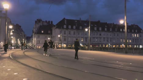 Stadt-Besancon-In-Der-Franche-Comté-Nachtleben-Mit-Menschen,-Die-über-Eine-Fußgängerbrücke-Mit-Straßenbahnschienen-Und-Straßenlaternen-Laufen