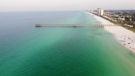 Blue-green-turquoise-water-at-Panama-city-beach-Gulf-of-Mexico-Aerial-view-during-morning-dawn-with-fishing-pier-and-hotel-resort-building-in-the-background