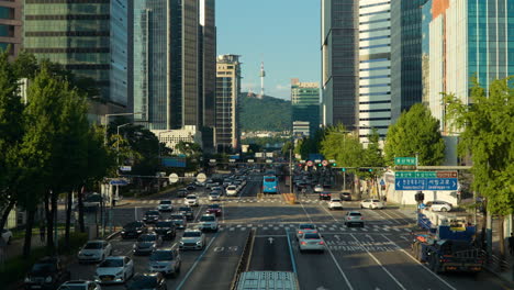 Estación-Sinyongsan-En-El-Centro-De-Seúl,-Tráfico-Intenso-En-La-Carretera-Hangang-daero-Con-Altos-Edificios-De-Oficinas-Alrededor-Y-Vista-De-La-Torre-N-Namsan---Vista-Elevada-Durante-El-Día---Alejar-La-Revelación