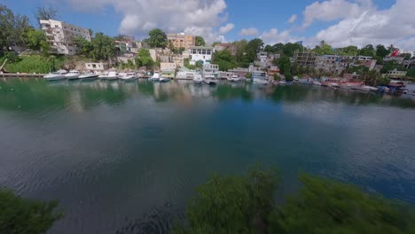 Aerial-fpv-flight-above-tropical-river-with-parking-boats-and-city-of-Romana-in-background,-Dominican-Republic