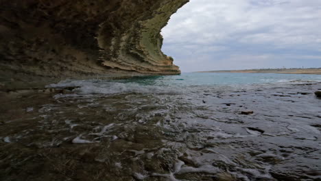Serenidad-En-Cámara-Lenta-De-Aguas-Turquesas-Rodando-Suavemente-Sobre-Una-Superficie-Rocosa-Plana-En-Una-Cueva,-Malta