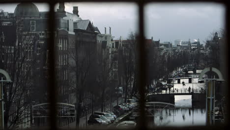 Winter-view-through-window-to-Amsterdam-canal-with-bridge-and-old-historic-houses