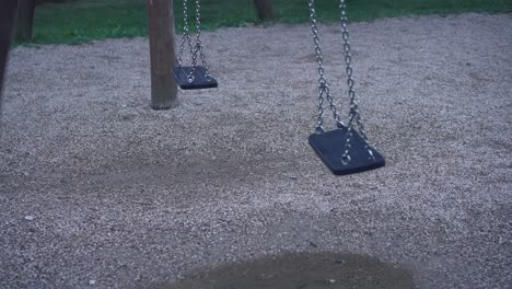 High-angle-shot-over-empty-swings-with-one-of-the-swing-moving-in-the-wind-in-a-playground-at-daytime