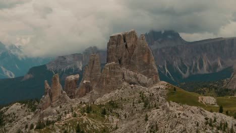Parallax-drone-shot-massive-rock-formations-with-distant-tall-mountains-in-the-background,-green-forest-at-the-bottom,-cloudy-day,-cinematic-color-grade