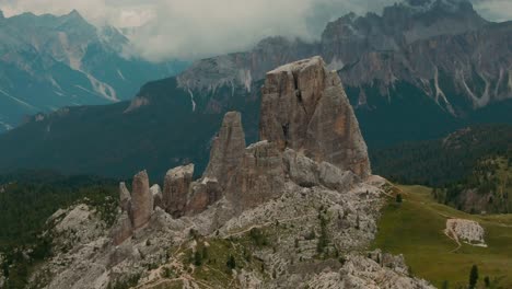 Tracking-drone-shot-massive-rock-formations-with-distant-tall-mountains-in-the-background,-green-forest-at-the-bottom,-cloudy-day,-cinematic-color-grade