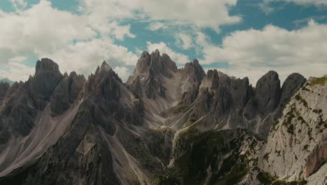 Drone-shot-with-tall-steep-rocky-mountains-and-partly-clouded-sky-in-the-background,-hiking-in-the-Alps,-majestic-landscape,-cinematic-color-grade