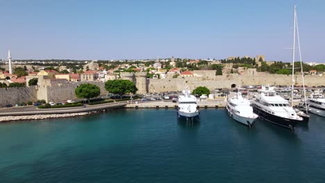 Docked-boats-and-yachts-in-Kolona-harbor-and-medieval-city-defense-wall,-aerial
