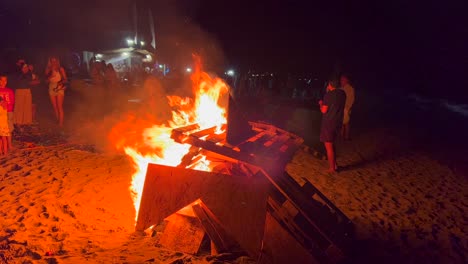 Tradicional-Festival-De-Verano-Con-Hogueras-En-La-Playa-En-La-Celebración-De-San-Juan-En-Marbella,-España,-Amigos-Y-Familiares-Disfrutando-De-Una-Fiesta-Divertida,-Un-Gran-Fuego-Ardiente-Y-Llamas-Calientes-Por-La-Noche,-Tomas-De-4k