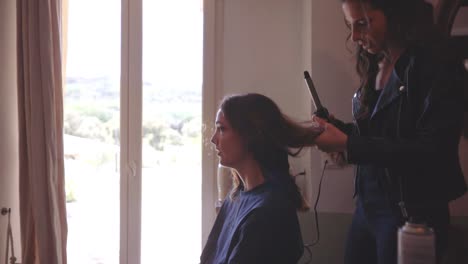 Mädchen-Sitzt-Im-Zimmer-Und-Lässt-Sich-Von-Einem-Friseur-Mit-Einem-Lockenstab-Die-Haare-Frisieren