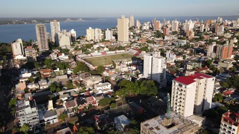 Luftaufnahme-Der-Küstenstadt-Posadas-Misiones-Argentinien,-Drohnenaufnahme-Einer-Dicht-Besiedelten-Küstenstadt-Bei-Wolkenverhangenem-Himmel-Mit-Fußballstadion