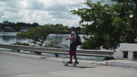 Young-man-riding-with-skateboard-along-coastal-road,-slow-motion