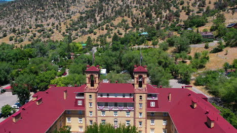 Aerial-view-around-flags-on-top-of-the-Hotel-Colorado-in-Glenwood-springs,-sunny,-summer-day-in-Colorado,-USA