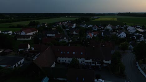 As-sun-sets-in-the-distance-night-surrounds-a-small-German-town,-aerial