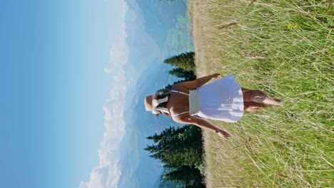 Pretty-woman-walking-in-high-grass-on-slope-of-alp-mountains-at-summer-day,-slow-motion---vertical-shot