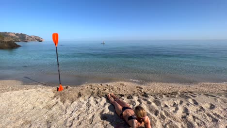 Sporty-girl-with-abs-laying-on-the-beach-with-kayak-puddle-in-sand-with-sea-view-in-Nerja-Malaga-Spain,-sunny-day,-fun-vacation-activity,-adventurous-water-sport,-4K-shot