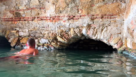 Roman-Baths-of-Casares-Manilva,-people-swimming-in-natural-spring-healing-sulfur-water-in-Spain,-good-health-benefits,-4K-shot