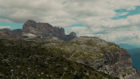 Drone-shot-with-tall-steep-rocky-mountains-and-partly-clouded-sky-in-the-background,-cinematic-color-grade