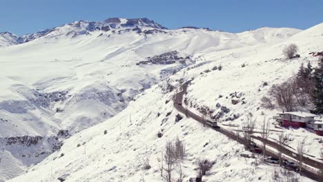 Luftaufnahme-Der-Steilen-Straße,-Die-Von-Der-Winterlichen-Gebirgslandschaft-Farellones-Zum-Exklusiven-Skigebiet-La-Parva-Führt