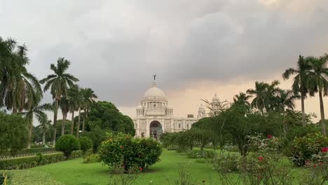 Toma-De-Monumento-De-Mármol-Blanco---Monumento-A-Victoria-En-La-Distancia,-Rodeado-De-Vegetación-Verde-En-Kolkata,-Bengala-Occidental,-India-En-Una-Tarde-Nublada