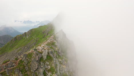Cinematic-revealing-drone-shot-mountain-ridge-through-the-clouds,-Fløya-and-Djevelporten-above-Svolvær-in-Lofoten,-Norway,-aerial-footage
