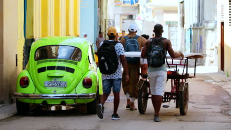 Cuban-Locals-Pushing-Cart-Past-Green-Parked-Retro-Volkswagen-Beetle-In-Havana-Street