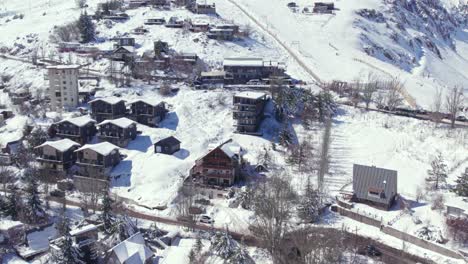 Orbiting-drone-shot-of-European-style-houses-and-cabins-of-the-snow-filled-village-of-Farellones-on-a-sunny,-snowy-day,-Chile